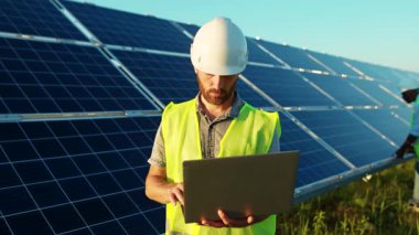 Portre genç adam dizüstü bilgisayar kullanıyor. Güneş pillerinin yakınındaki kameraya bak. Günışığı teknolojisinde yenilenebilir elektrik işçisi.