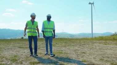Yürüyen mühendisler tarlalardaki yel değirmenlerinin yanında tartışıyorlar ekip işgücü işbirliği rüzgar enerjisi tarım teknisyenleri yavaş çekim konuşuyor.