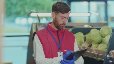 Genç satıcının portresi süpermarkette deftere yazıyor. Kamera, sebze, güzel, taze ürünler, perakende, yavaş çekim.