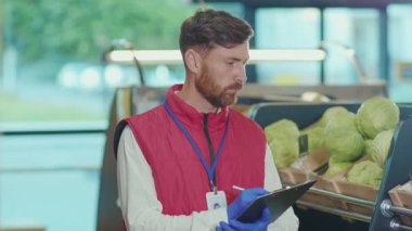 Ciddi genç satıcı, süpermarkette çek yazar. Sebze işi. Güzel, taze, perakende satış mağazası.