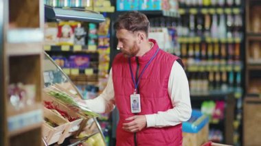 Kapalı gişe oynayan genç adam sebzeleri süpermarketin raflarına koyuyor sebzeleri kontrol ediyor güzel, taze, perakende satış yapan, yavaş çekim yapan bir dükkan.