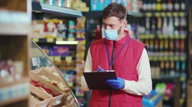 Maskeli genç satıcı süpermarket sebze işinde kontrol ediliyor. Güzel, taze, perakende satış mağazası yavaş çekim.