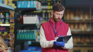 Çekici genç satıcı, süpermarkette bir deftere yazıyor. Kamera, ciddi sebze işi. Güzel, taze, perakende satış mağazası, yavaş çekim.