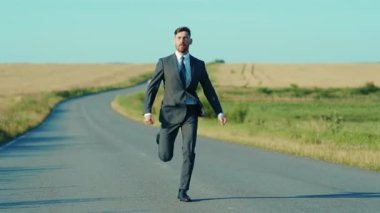 Kendine güvenen işadamı koşar, buğday tarlası özgürlük kavramının yakınındaki ceketli kır yolunu kaldırır.