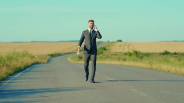 Mutlu iş adamı akıllı telefonlu bir kır yolunda konuşuyor buğday tarlası özgürlük kavramının yanında açık hava yakışıklı kazanan zarif, yavaş çekim