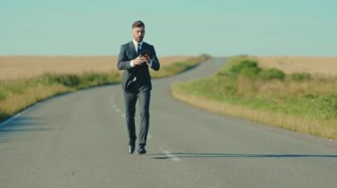 Kendine güvenen bir işadamı akıllı telefon kullanır. Ceketini çıkarır, kır yolunda koşar. Açık hava özgürlük kavramının yanında koşar.