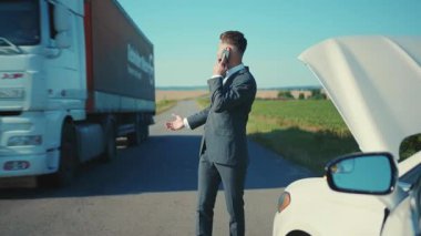 Sinirli işadamı telefonda bozuk arabanın yanında konuşuyor. Kaput yolunu açtı. Stres sorununun çözümüne yardım etti.