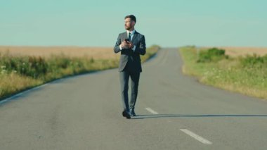 Çekici iş adamı akıllı telefon yürüyüşü yapar buğday tarlası özgürlük kavramının yanında tek başına kır yolunda koşar. Yakışıklı, yavaş çekim kazanır.