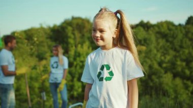 Çevreye gülümseyen şirin bir kızın portresi kameraya gülümseyen beyaz bir tişört giyip geri dönüşüm sembolü olarak aile ekolojisi ekolojik toplum eldivenleri yavaş çekim