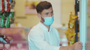 Maskeli adam süpermarkette duruyor. Kameraya bak. Müşteri kiti, dükkan, market, market, perakende, yavaş çekim.