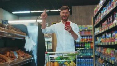 NEW YORK - 19 Nisan 2020: Markette yürüyen mutlu bir adam telefon müşteri listesindeki alışveriş listesine bakıyor.