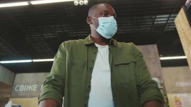 Afrika kökenli Amerikalı adam maskeli, Covid-19 Coronavirus salgını sırasında süpermarkette geziniyor.