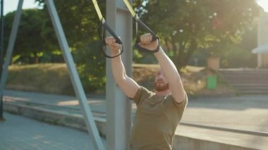 NEW YORK - 5 Eylül 2020: Güneşli bir günde stadyumda trx fitness halatıyla vücut egzersizleri yapan çekici genç adam spor kıyafetlerini yavaş çekimde çalıştırıyor.