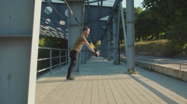 NEW YORK - 5 Eylül 2020: Trx fitness halat vücut egzersizleri ile çalışan açık hava genç adam güneşli bir günde stadyumda kas sporu antrenmanı yapıyor.