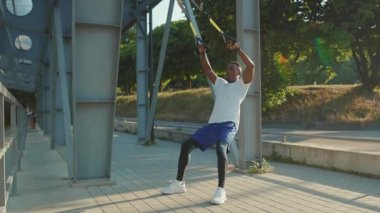 NEW YORK - 5 Eylül 2020: Trx fitness halatıyla çalışan yakışıklı Afro-amerikalı adam stadyum kaslı spor kıyafetleri spor antrenmanı ağır çekimde vücut egzersizleri yapıyor.