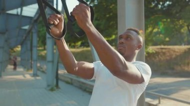 NEW YORK - 5 Eylül 2020: Trx fitness halatı ile çalışan genç Afrikalı Amerikalı adam stadyum kas antrenmanlarında vücut egzersizleri spor spor kıyafetleri yavaş çekim egzersizleri yapıyor