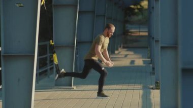 NEW YORK - 5 Eylül 2020: Güneşli bir günde, spor kıyafetleri spor antrenörleri spor antrenmanında trx fitness halat vücut egzersizleri yapan genç adam yavaş çekim spor antrenmanlarını kapatıyor