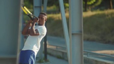 NEW YORK - 5 Eylül 2020: Trx fitness halatıyla çalışan genç Afrikalı Amerikalı adam stadyum kaslı spor kıyafetleri spor antrenmanında vücut egzersizleri yapıyor.