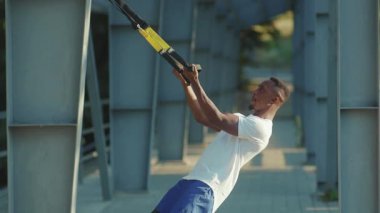 NEW YORK - 5 Eylül 2020: Trx fitness halatıyla çalışan yakışıklı Afro-amerikalı adam stadyum kaslı spor kıyafetleri spor antrenmanı ağır çekimde vücut egzersizleri yapıyor.