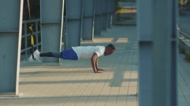 NEW YORK - 5 Eylül 2020: Trx fitness halatı ile çalışan güçlü ve yakışıklı Afro-Amerikalı adam stadyumda vücut egzersizleri yapıyor.