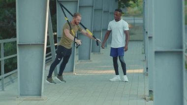 NEW YORK - 5 Eylül 2020: Trx fitness halatıyla çalışan iki genç adamı kapatın stadyumdaki Afrika kökenli Amerikan spor giyim spor giyim spor giyim spor kıyafetleri ağır çekimde vücut egzersizleri yapın
