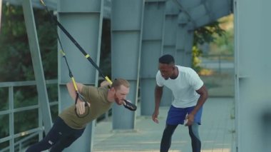 NEW YORK - 5 Eylül 2020: Trx fitness halatı ile spor yapan iki genç adam stadyum Afrika kökenli Amerikan spor giyim spor giyim spor kıyafetleri ağır çekimde vücut egzersizleri yapıyor.