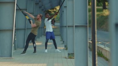 NEW YORK - 5 Eylül 2020: Trx fitness ipi ile çalışan genç yakışıklı erkekler stadyum kaslı Afrika kökenli Amerikan spor giyim spor giyim spor kıyafetleri ağır çekimde vücut egzersizleri yapıyorlar