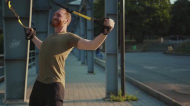 NEW YORK - 5 Eylül 2020: Çekici genç adam, başka bir Afrikalı Amerikalıyı, trx fitness halatıyla, açık havada vücut egzersizleriyle, stadyum kaslı spor kıyafetleri spor kıyafetleri spor salonlarında, ağır çekimde çalışmaya teşvik etti.