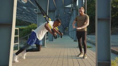NEW YORK - 5 Eylül 2020: Yakışıklı genç adam başka bir Afrikalı Amerikalıyı spor kıyafetleri spor antrenmanlarında trx fitness halatıyla dışarıda vücut egzersizleriyle motive etti