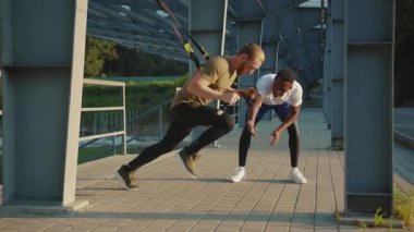 NEW YORK - 5 Eylül 2020: Yaklaşan genç adam, başka bir Afrikalı Amerikalıyı, trx fitness halatıyla, açık havada vücut egzersizleriyle, stadyum kaslı spor kıyafetleri spor kıyafetleri spor antrenmanlarında, yavaş çekimde çalışmaya teşvik etti.