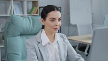 Ofiste bilgisayar ekranına bakan ciddi bir iş kadınının portresi. Klavyede yazan kadın yönetici, kameraya bakıyor ve gülümsüyor..