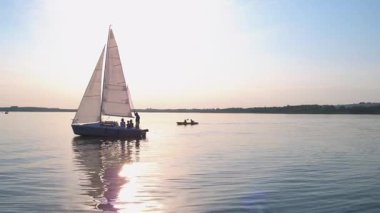 Küçük bir yatla gezen bir grup mutlu genç turist. Güzel göl manzarası, durgun su manzaralı gökyüzü ve kıyılar..