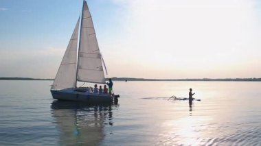 Yüzen turistlerle dolu güzel sakin bir nehir manzarası. Küçük beyaz bir yatla yelken açan genç bir şirket. Yat aktivitesi. Yaz tatili.