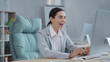 Bilgisayarla masada oturan, resmi kıyafetli, heyecanlı, beyaz bir kadının portresi. Mutlu güzel iş kadını bilgisayarda harika haberler okuyor, mutlu hissediyor. Başarı. İş yeri, ofis. Kapalı