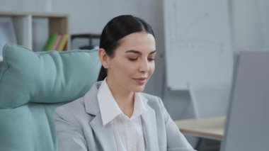 Ofiste bilgisayarla çalışan resmi kıyafetli hoş görünümlü beyaz bir kadının yakın çekim görüntüleri. Kameraya bakan çekici, gülümseyen bir kız fotoğrafı. Bayan menajer. Mesleğiniz. Kapalı