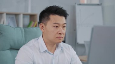 Ciddi bir ofis çalışanının portresi. Beyaz gömlekli, bilgisayarın başında oturmuş kameraya bakıyor. Ofiste resmi giyinmiş yetişkin bir Asyalı. Açık alan, gündüz. İş için. Kapalı