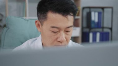 İş yerinde oturup bilgisayar kullanan iyi giyimli Asyalı adamın yakın plan portresi. İyi görünümlü Çinli ciddi bir ofis çalışanı klavyede yazı yazıyor. İş günü. İçeride. İş konsepti. Kariyer