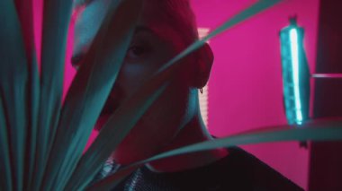 Portre genç stil gay adam pembe arka plandaki yaprakların arasından kameraya bak