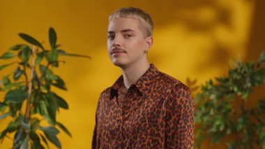 Çekici eşcinsel adam kameraya bakar sarı arka plandaki yeşil yapraklara gülümser.