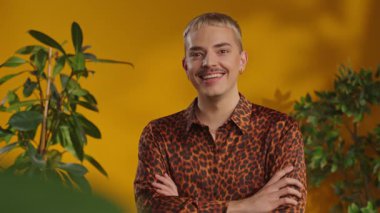 Gülümseyen mutlu eşcinsel portresi sarı arka plandaki yeşil yapraklara bakıyor.