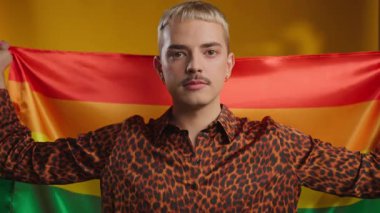 Omzunda Lgbt bayrağı tutan adamın portresi sarı arka plandaki kameraya bakar