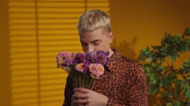 Şirin adam buketi tutuyor kameraya gülümsüyor şık gömlekle. Sarı arkaplan