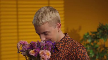 Mutlu adam elinde buket tutarken kameraya gülümsüyor. Sarı arkaplan