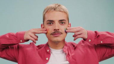 Gülümseyen genç eşcinsel adam kameraya bakar ve yüzüne Lgbt bayrağı çizer.