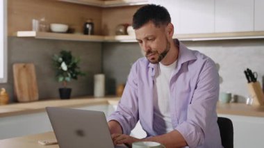Gündelik giysiler içinde güzel görünümlü genç adam dizüstü bilgisayarda oturuyor, dairenin mutfağında klavyeye yazı yazıyor. Yorgun adamın portresi doğrudan kameraya bakıyor. Stres, yüksek tansiyon, baş ağrısı. Bağımsız