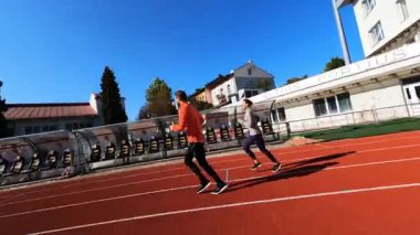 FPV, profesyonel genç sporcu ve sporcunun stadyumda koşu antrenmanında birlikte koştuğunu gösteriyor. Aktif yaşam tarzı. Sağlık Hizmetleri.