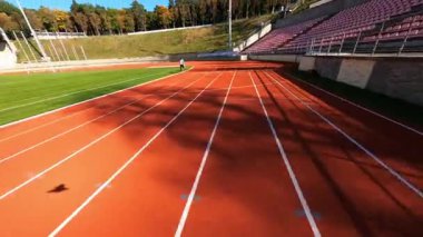 Çağdaş koşu stadyumunun üzerinde manevra kabiliyeti olan FPV uçuşu. Spor sahasında koşan profesyonel genç erkek sporcu..