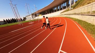 Takım çalışması. Stadyumda birlikte koşup gelecekteki maratona hazırlanan kararlı, genç beyaz bir çift. Sağlıklı bir yaşam tarzı. Koşucular. Spor haberleri. FPV görünümleri.