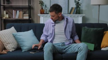 Kapatın genç adam telefonu kullandıktan sonra kitap okuyun. Ekrana bakın. Evdeki kanepede oturup ağlayın. Portre. İletişim işadamı sosyal medyada sohbet ediyor. Kapatın. Portre. Yavaş çekim