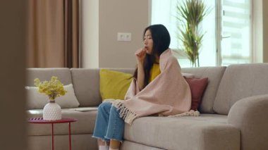 Kanepede battaniyeli oturan Asyalı genç kadın kendini hasta hissediyor. Salgın. Coronavirus. Enfeksiyon kapmış hastalık stres altında. Hastalık. Yavaş çekim